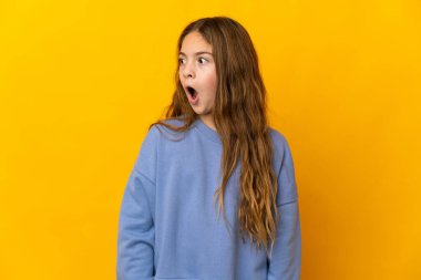 İzole edilmiş sarı arka plan üzerinde çocuk yan tarafa bakarken sürpriz jest yapıyor