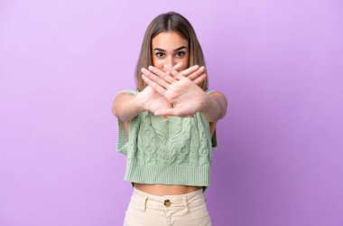 Mor arka planda izole edilmiş genç beyaz kadın bir hareketi durdurmak için eliyle jest yapıyor.