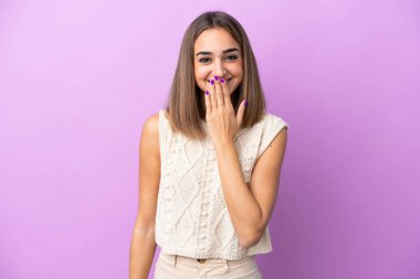 Mor arka planda izole edilmiş genç beyaz kadın mutlu ve gülümseyerek elleri ile ağzını kapatıyor.