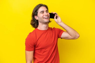 Beyaz tenli yakışıklı adam sarı arka planda izole edilmiş cep telefonuyla sohbet ediyor.