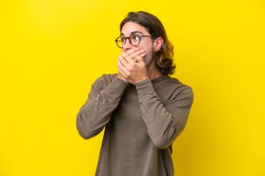 Beyaz tenli yakışıklı adam sarı arka planda izole edilmiş ağzını kapatıyor ve yan tarafa bakıyor.