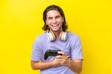 Sarı arka planda izole edilmiş bir bilgisayar oyunu kontrolörüyle oynayan yakışıklı beyaz adam çok gülümsüyor.