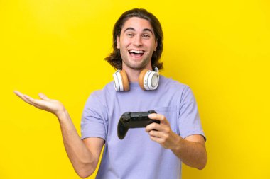 Yakışıklı, beyaz bir adam, sarı arka planda izole edilmiş bir bilgisayar oyunu kontrolörüyle oynuyor.