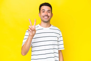 Sarı arka plan üzerinde genç yakışıklı adam gülümsüyor ve zafer işareti gösteriyor.