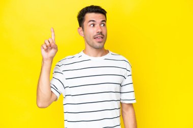 Soyutlanmış sarı arka planı olan genç yakışıklı bir adam parmağını kaldırarak çözümü bulmaya çalışıyor.