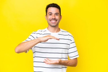 İzole edilmiş sarı arka planda genç yakışıklı bir adam. Avucunun içinde hayali bir ilan tutuyor.