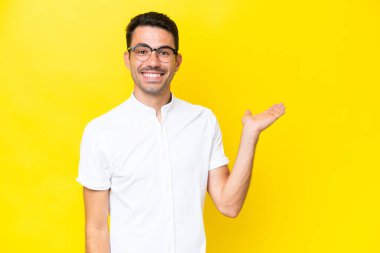 İzole edilmiş sarı arka planda genç yakışıklı bir adam. Avucunun içinde hayali bir ilan tutuyor.