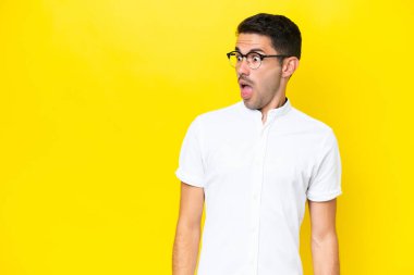 Sarı arka plan üzerinde genç yakışıklı bir adam. Yan tarafa bakarken sürpriz jest yapıyor.