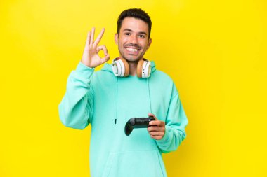 Genç yakışıklı bir adam, izole edilmiş duvarın üzerinde bilgisayar oyunu kontrolörüyle oynuyor. Parmaklarıyla tamam işareti gösteriyor.