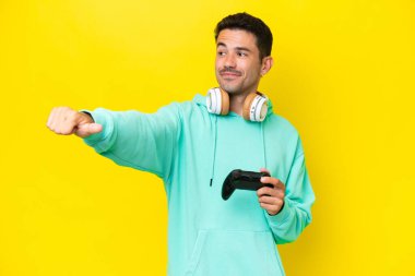 Genç yakışıklı bir adam, izole edilmiş duvarın üzerinde bilgisayar oyunu kontrolörüyle oynuyor ve baş parmak işareti yapıyor.