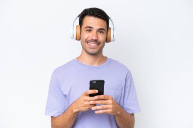 Genç yakışıklı adam izole edilmiş beyaz arka planda müzik dinliyor ve önüne bakıyor.