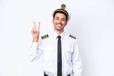 İzole edilmiş beyaz arka planda gülümseyen ve zafer işareti gösteren bir uçak pilotu.