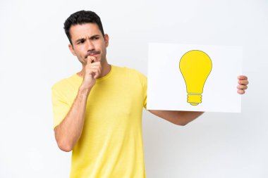 Soyutlanmış beyaz arka plan üzerinde genç yakışıklı bir adam elinde bir afiş tutuyor ve düşünüyor.