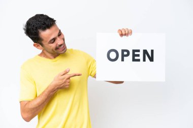 İzole edilmiş beyaz arka planda genç yakışıklı bir adam elinde açık yazılı bir pankart tutuyor ve onu işaret ediyor.