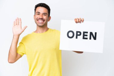 İzole edilmiş beyaz arka planda genç yakışıklı bir adam. Elinde açık yazılı bir pankart var ve selam veriyor.