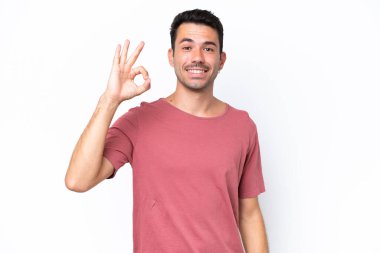 İzole edilmiş beyaz arka planda genç yakışıklı adam parmaklarıyla işaret veriyor.