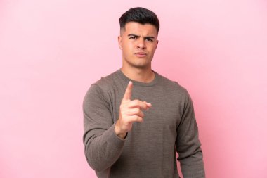 Pembe arka planda izole edilmiş genç beyaz adam hayal kırıklığına uğramış ve ön tarafı işaret ediyor.