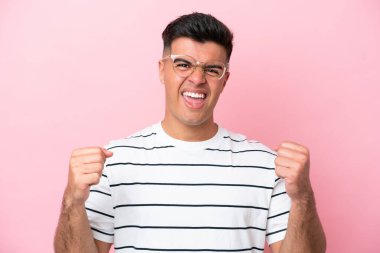 Pembe arka planda, gözlüklü ve zaferi kutlayan beyaz tenli yakışıklı bir adam.