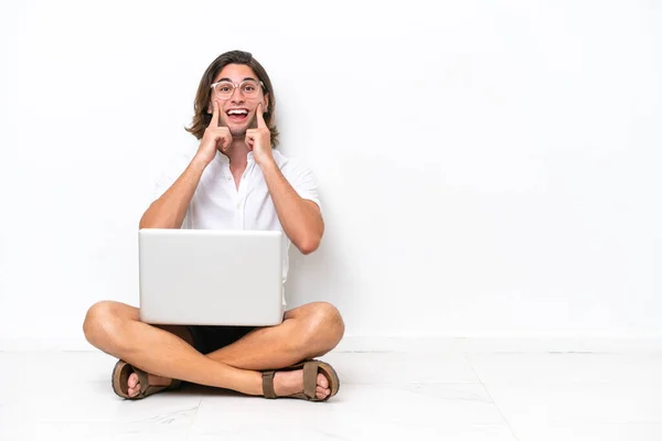 年轻英俊的男人 拿着笔记本电脑坐在地板上 被白色的背景隔离着 带着愉快的笑容笑着 — 图库照片