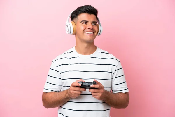 잘생긴 남자가 비디오 컨트롤러를 가지고 분홍색 배경에 엉덩이에 올리고 웃으며 — 스톡 사진