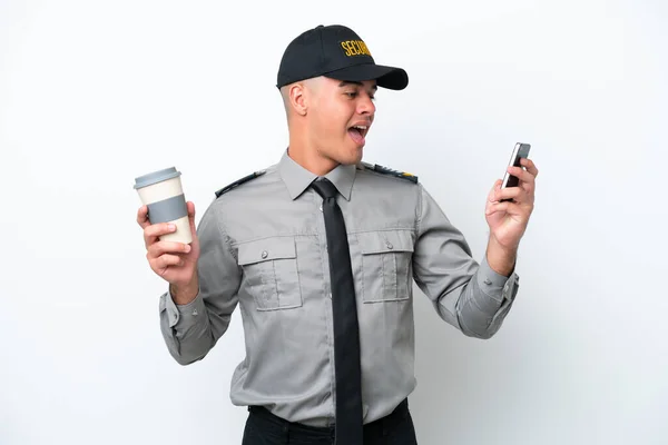 Young caucasian security man isolated on white background holding coffee to take away and a mobile