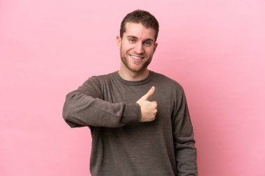 Pembe arka planda izole edilmiş genç beyaz bir adam baş parmak hareketi yapıyor.