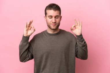 Zen pozisyonunda pembe arka planda izole edilmiş genç beyaz bir adam.