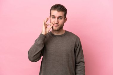 Pembe arka planda izole edilmiş genç beyaz adam sessizlik işareti gösteriyor.