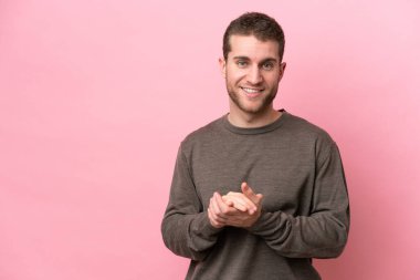 Pembe arka planda izole edilmiş genç beyaz adam alkışlıyor.