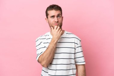 Pembe arka planda izole edilmiş genç beyaz adamın şüpheleri var.