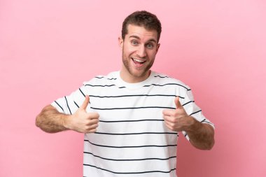 Pembe arka planda izole edilmiş genç beyaz bir adam baş parmak hareketi yapıyor.