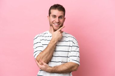Pembe arka planda izole edilmiş genç beyaz adam mutlu ve gülümsüyor.