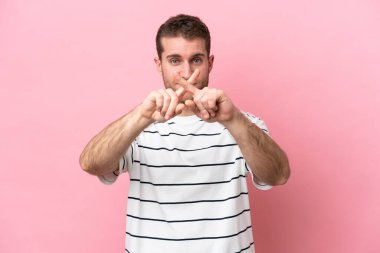 Pembe arka planda izole edilmiş genç beyaz adam bir hareketi durdurmak için eliyle jest yapıyor.