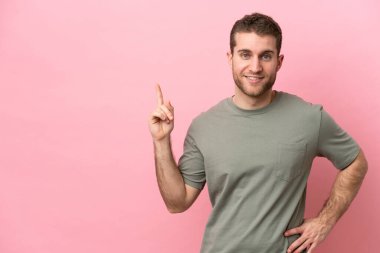 Pembe arka planda izole edilmiş genç beyaz adam en iyinin işareti olarak parmağını kaldırıyor.