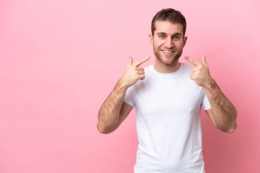 Pembe arka planda izole edilmiş genç beyaz bir adam baş parmak hareketi yapıyor.