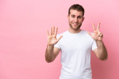 Pembe arka planda izole edilmiş genç beyaz adam parmaklarıyla sekizi sayıyor.