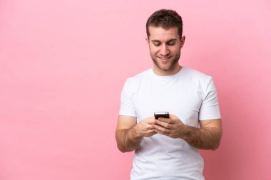 Pembe arka planda izole edilmiş genç beyaz adam cep telefonuyla bir mesaj gönderiyor.