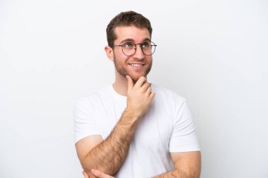 Beyaz arka planda gözlüklü ve düşünen genç beyaz bir adam.