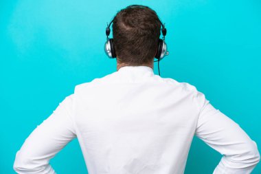 Tele pazarlamacı beyaz adam arka planda mavi arka planda izole edilmiş bir kulaklıkla çalışıyor.