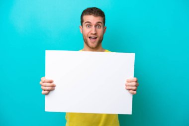 Young caucasian man isolated on blue background holding an empty placard with happy expression