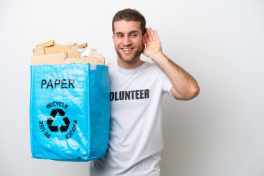 Beyaz arka planda izole edilmiş bir şekilde geri dönüşüm için elinde kağıt dolu bir torba tutan beyaz bir adam elini kulağına koyarak bir şey dinliyor.