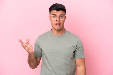 Pembe arka planda izole edilmiş beyaz, yakışıklı genç bir adam şüpheli hareketler yapıyor.