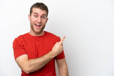 Beyaz arka planda izole edilmiş genç beyaz adam şaşırmış ve işaret ediyor.