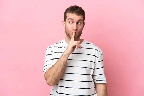 ピンクの背景に孤立した若い白人男性は 沈黙のジェスチャーの兆候を示す指を口に入れる — ストック写真