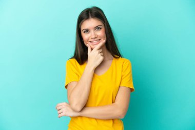 Mavi arka planda izole edilmiş genç beyaz kadın mutlu ve gülümsüyor.