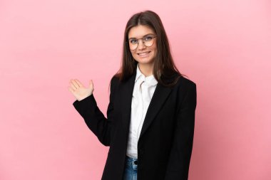 Pembe arka planda izole edilmiş genç beyaz kadın, davet edilmek için ellerini yana uzatıyor.