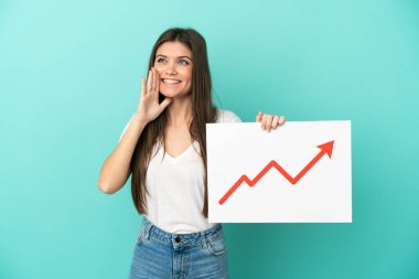 Mavi arka planda izole edilmiş genç beyaz bir kadın elinde büyüyen bir istatistik okunun sembolü olan ve bağıran bir tabela tutuyor.