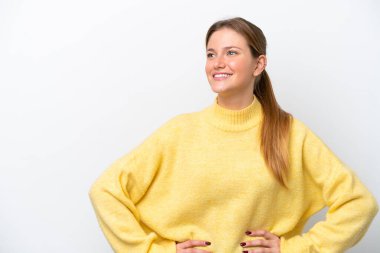 Beyaz arka planda izole edilmiş genç beyaz kadın kolları kalçasında ve gülümsüyor.