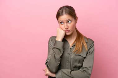 Pembe arka planda soyutlanmış, yorgun ve sıkılmış bir ifadeyle genç beyaz kadın.