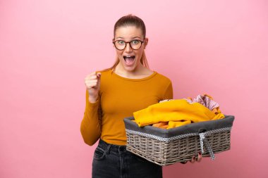 Pembe arka planda izole edilmiş çamaşır sepeti tutan beyaz bir kadın galibiyeti kutluyor.